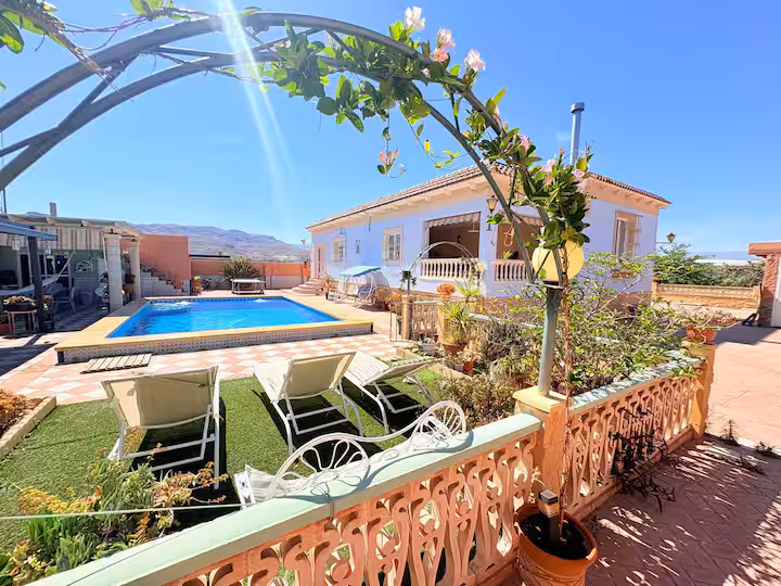 Villa blanca y azul con piscina, tumbonas y terraza entre jardines, en Pechina
